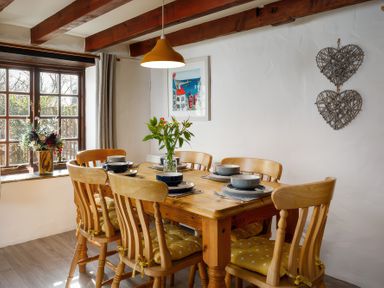 A dining room with a wooden table and six chairs with yellow cushions and tableware at Pond Meadow Warbstow