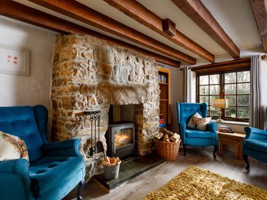 A living room with blue armchairs a stone fireplace a basket with firewood and a window at Little Leighs in Warbstow