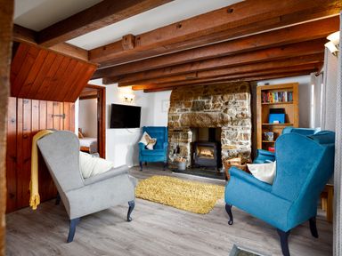 A living room with wooden beams a stone fireplace and upholstered armchairs at Little Leighs in Warbstow