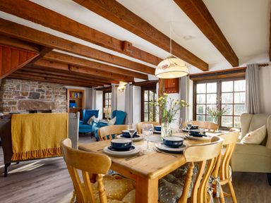 A dining table set with plates bowls and glasses in a room with wooden beams stone fireplace and blue armchairs at Little Leighs Warbstow