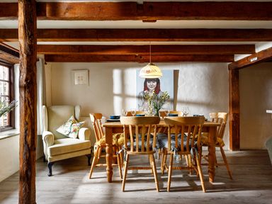 A dining room with a wooden table and chairs a cushioned armchair and a painting on the wall at Little Leighs Warbstow