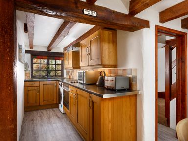 A kitchen with wooden cabinets a microwave toaster and kettle under exposed wooden beams at Little Leighs in Warbstow
