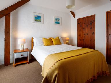 A bedroom with a double bed with yellow cushions and throw and two bedside tables with lamps at Little Leighs in Warbstow