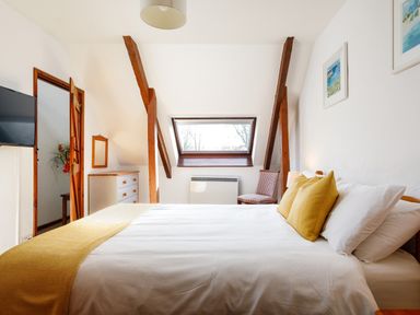 A bedroom with a bed with yellow pillows and blanket a chair a dresser and a window at Little Leighs in Warbstow