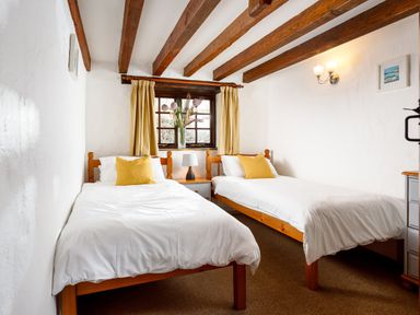 A bedroom with two single beds and a window with curtains at Little Leighs Warbstow