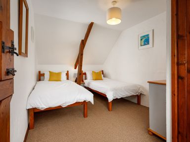 A bedroom with two single beds with yellow pillows a wooden beam and a dresser at Little Leighs in Warbstow