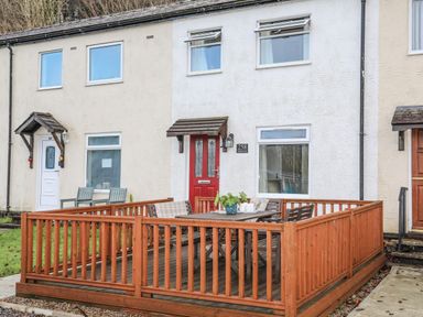 A front porch with wooden railing and outdoor table and chairs at Eirlys in Caeathro near Caernarfon