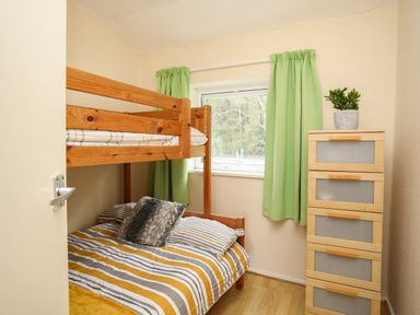 A small bedroom with a bunk bed green curtains and a chest of drawers with a plant on top at Eirlys in Caeathro near Caernarfon