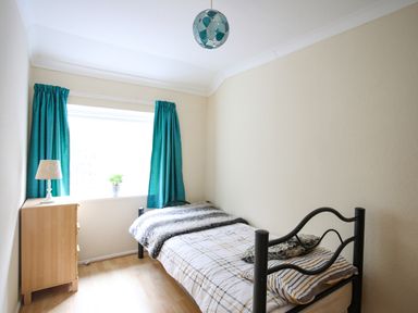 A small bedroom with a single bed a wooden chest of drawers a lamp and teal curtains at Eirlys in Caeathro near Caernarfon