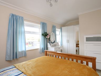 A bedroom with a wooden bed yellow blanket blue curtains white wardrobe and dressing table at Eirlys Caeathro near Caernarfon