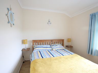 A bedroom with a wooden bed and striped bedspread with yellow lamps on wall shelves at Eirlys in Caeathro near Caernarfon