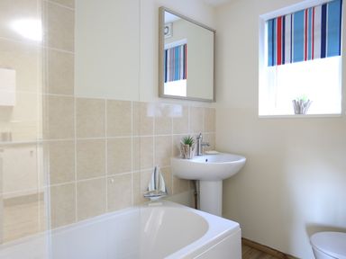 A bathroom with a bathtub a pedestal sink mirror and a window with a striped blind at Eirlys in Caeathro near Caernarfon