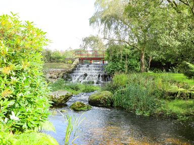 A small stream with rocks and greenery flowing under a red bridge at Eirlys in Caeathro near Caernarfon