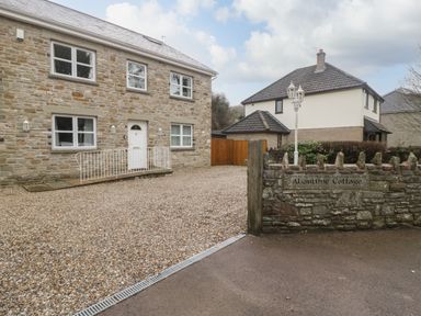 Stone cottage with white door and windows gravel driveway and stone wall with a sign in front at About Time Cottage in Parkend