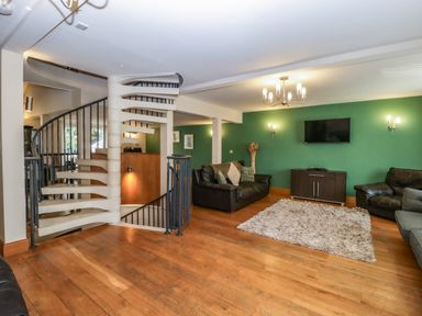 A living room with a white spiral staircase leather sofas wooden floor and a green wall with a TV at About Time Cottage in Parkend
