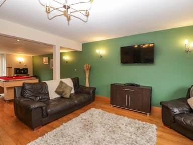A living room with two black leather sofas a wall-mounted TV a dark wooden cabinet a green wall and a pool table at About Time Cottage in Parkend