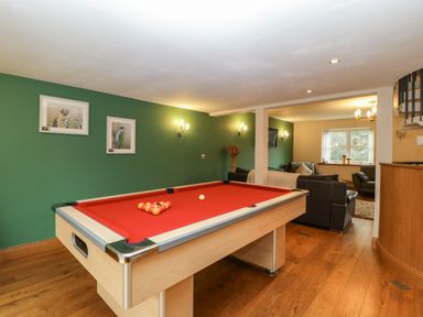 A room with a red pool table, green walls, wall lights, framed pictures, wooden floor, and a seating area at About Time Cottage in Parkend