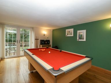 A game room with a red pool table wooden floor and glass doors leading outside at About Time Cottage in Parkend