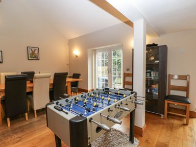 A room with a foosball table wooden dining table with chairs and glass cabinet at About Time Cottage in Parkend