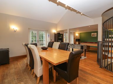 A dining room with a wooden table and mixed black and white chairs a foosball table and pool table near a green wall and spiral staircase at About Time Cottage in Parkend