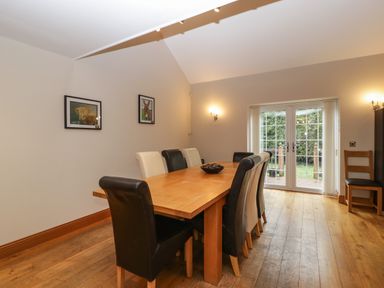 A dining room with a wooden table and eight chairs near glass doors at About Time Cottage in Parkend