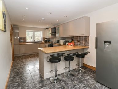 A kitchen with a breakfast bar and three stools a refrigerator and cabinets at About Time Cottage in Parkend