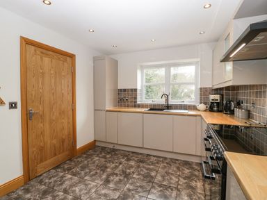 A kitchen with cabinets a stove a window and a wooden door at About Time Cottage in Parkend