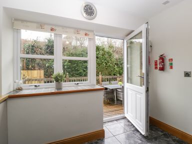 A kitchen door open to a wooden deck with table and chairs and a window with plants on the sill at About Time Cottage in Parkend