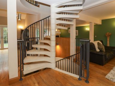 An interior space with a spiral staircase wooden floors green walls and a black sofa at About Time Cottage in Parkend