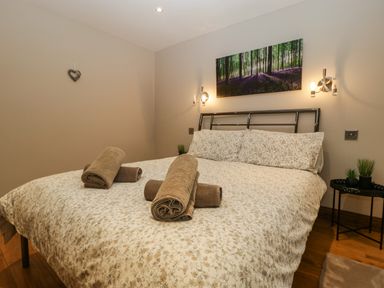 A bedroom with a double bed with floral bedding rolled towels on the bed wall lights and a forest picture above the bed at About Time Cottage in Parkend