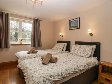 A bedroom with two single beds side by side with floral bedding and folded towels on them a window with curtains and a framed picture of sheep on the wall at About Time Cottage in Parkend