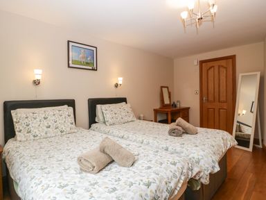 A bedroom with two beds with floral bedding towels on beds a wooden door a dressing table and a standing mirror at About Time Cottage in Parkend