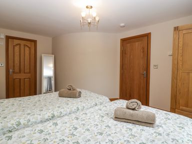 A bedroom with two single beds each with folded towels a standing mirror and three wooden doors at About Time Cottage in Parkend