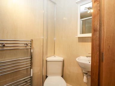 A small bathroom with a corner toilet a wall-mounted sink a mirror and a towel radiator at About Time Cottage in Parkend