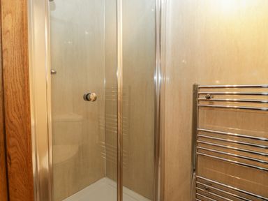 A bathroom shower enclosure with glass doors and a chrome towel radiator at About Time Cottage in Parkend
