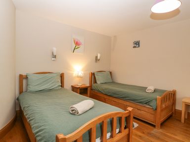 A bedroom with two single wooden beds with green bedding and rolled towels on each bed at About Time Cottage in Parkend
