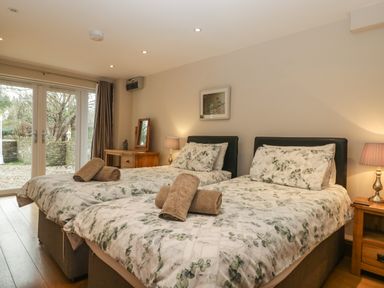 A bedroom with two single beds with patterned bedding and rolled towels on them with wooden nightstands and lamps and a dresser with a mirror and glass doors leading outside at About Time Cottage in Parkend