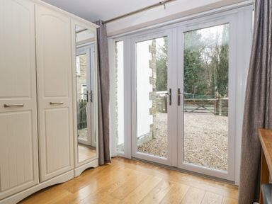 A room with wooden floor cabinets with mirrored doors and large glass doors opening to a gravel driveway at About Time Cottage in Parkend