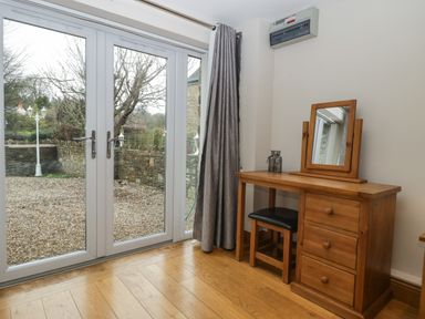 A wooden dressing table with a mirror and stool near glass doors with stone wall outside at About Time Cottage in Parkend
