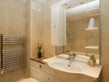A bathroom with a white sink and cabinet a mirror a silver towel rack and a small plant at About Time Cottage in Parkend