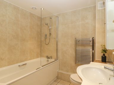 A bathroom with a bathtub shower combination a towel rack sink and a small plant at About Time Cottage Parkend