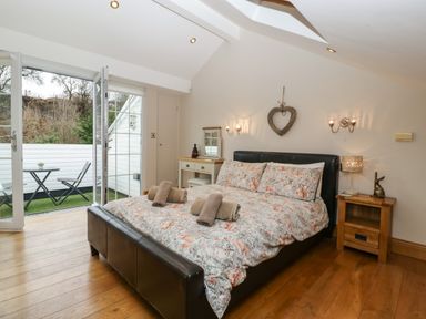 A bedroom with a double bed and floral bedding a small wooden bedside table and a vanity with an open door to a balcony at About Time Cottage in Parkend