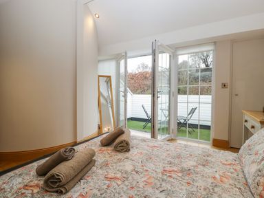 A bedroom with a bed with floral bedding and folded towels overlooking a balcony with chairs and a table at About Time Cottage in Parkend