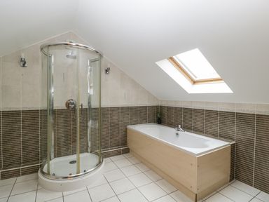 A bathroom with a corner glass shower enclosure and a bathtub under a skylight at About Time Cottage in Parkend