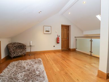 An attic space with wooden flooring a zebra patterned armchair a small glass side table a door and glass railing at About Time Cottage in Parkend