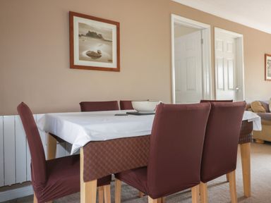 A dining room with a table covered with white and brown cloth and six brown chairs at Watergate Bay in Liskeard