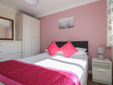 A bedroom with a double bed pink pillows and blanket white wardrobe and dresser at Watergate Bay in Liskeard