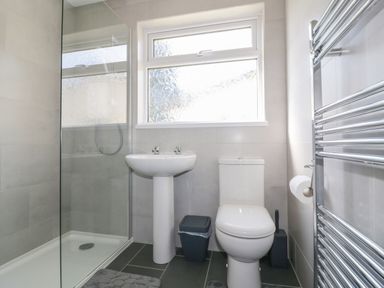 A bathroom with a shower area, a pedestal sink, a toilet, a trash bin, a toilet brush, and a heated towel rail at Watergate Bay in Liskeard