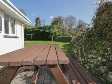 An outdoor area with a wooden picnic table lawn with rotary clotheslines and a stone wall covered with ivy at Watergate Bay in Liskeard