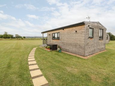A wooden cabin with a stone path and grass field at Cotswold View 1 in Honeybourne